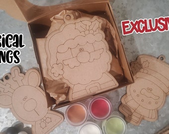 May include: A set of three unfinished wooden Christmas ornaments in a box with paint pots. The ornaments are a reindeer, Santa Claus, and a snowman. The text "Whimsical Inkling" and "SVG Laser Ready" are visible on the image. The text "EXCLUSIVE!" is visible in the top right corner of the image.