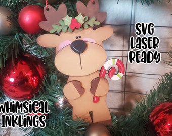 May include: A brown wooden reindeer ornament with a red candy cane, a green holly wreath with red berries, and the text "SVG Laser Ready" on a white background.