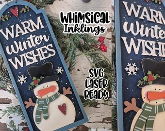 May include: Wooden sign with a snowman design. The sign reads "Warm Winter Wishes" in white lettering on a navy blue background. The snowman has a black hat, carrot nose, and green scarf. Decorative snowflakes and hearts are also present.