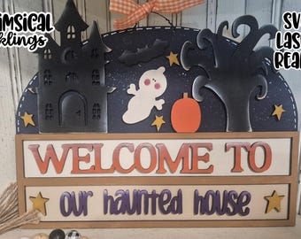 May include: A Halloween-themed wooden sign with a black haunted house, ghost, pumpkin, and tree cutouts. The sign reads "WELCOME TO our haunted house" in orange and purple letters. The background is dark blue with stars.