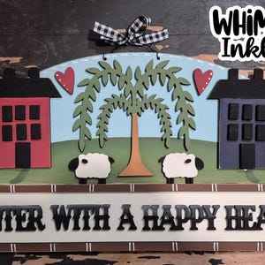 May include: A wooden sign with a whimsical design featuring two houses, a weeping willow tree, two sheep, and a banner that reads "Enter with a happy heart".