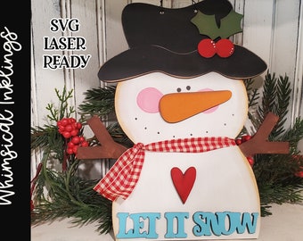 May include: A wooden snowman cutout with a black hat, red and white checkered scarf, and a red heart. The snowman has a carrot nose and is holding a brown stick arm. The words "Let It Snow" are written in blue letters on a blue background.