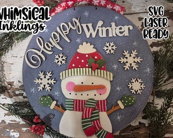 May include: A round, blue wooden sign with a snowman design and the words "Happy Winter". The snowman has a red hat, scarf, and mittens. White snowflakes are scattered around the snowman. The sign is decorated with a red ribbon.