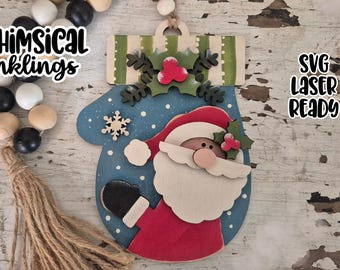 May include: A wooden Christmas mitten ornament featuring Santa Claus with a red suit, white beard, and a blue mitten. The ornament has a snowflake and holly accents. The text "WHIMSICAL Inkling" and "SVG Laser Ready" are visible.