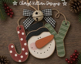 May include: A wooden holiday ornament spelling JOY with a snowman face as the letter O. The J is red with white polka dots, the Y is green with white stripes, and the snowman wears a black hat and orange nose. A buffalo check bow sits above.
