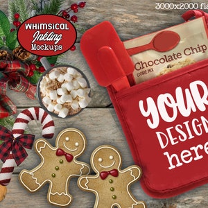 May include: Red oven mitt with a pocket for a bag of chocolate chip cookie mix. The text "YOUR DESIGN here" is printed on the mitt. The image also includes a gingerbread man cookie, a candy cane, a mug of hot chocolate with marshmallows, and a red and black plaid ribbon.
