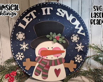 May include: A round, wooden snowman sign with the words "LET IT SNOW" in white letters. The snowman has a black top hat, carrot nose, and a red and green scarf. Decorative snowflakes surround the snowman on a navy blue background.
