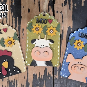 May include: Three wooden farm animal tags with scalloped edges. The tags feature a rooster, cow, and pig, each with a unique design and the sounds they make. The tags are decorated with sunflowers and the text "Cluck", "Moo", and "Oink".