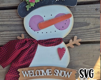 Könnte beinhalten: Holz-Schneemann-Dekoration mit schwarzem Hut, Karottennase und rot-schwarz kariertem Schal. Der Schneemann hat ein Banner mit der Aufschrift "WELCOME SNOW" und ein Herz auf der Brust. Der Text "SVG LASER READY" ist ebenfalls sichtbar.