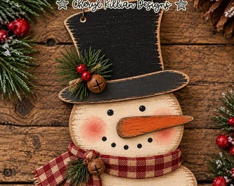 May include: A wooden snowman ornament featuring a black top hat, a carrot-shaped nose, and a red and white checkered scarf. The snowman has rosy cheeks and a dotted smile. Text reads Whimsical Inklings Cheryl Killian Designs laser ready svg.