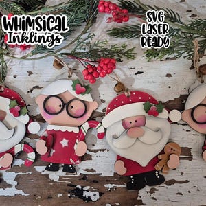 Puede incluir: Adornos navideños de madera con Papá Noel y Mamá Noel. Papá Noel lleva un gorro rojo y barba blanca. Mamá Noel lleva gafas y un vestido rojo. Los adornos están decorados con acebo y bastones de caramelo. El texto "Whimsical Inklings" es visible.