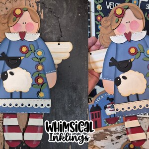 May include: A blue angel with wings, a white sheep, a black bird, and red and white striped legs. The angel is wearing a blue dress with white lace trim and flowers. The text "Whimsical Inkling" is in the bottom right corner. The text "SVG Laser Ready" is in the top right corner.