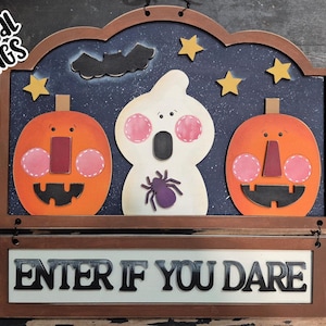 May include: A wooden Halloween sign featuring a ghost, two jack-o'-lanterns, and stars against a dark blue backdrop. The sign reads "Enter if you dare" and has an "SVG Laser Ready" label in the bottom right corner.