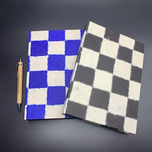 K&ouml;nnte beinhalten: Zwei Notizb&uuml;cher mit karierten Mustern. Ein Notizbuch hat blaue und wei&szlig;e Quadrate, das andere hat schwarze und wei&szlig;e Quadrate.