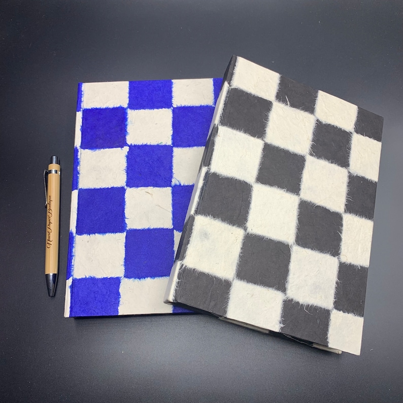 K&ouml;nnte beinhalten: Zwei Notizb&uuml;cher mit karierten Mustern. Ein Notizbuch hat blaue und wei&szlig;e Quadrate, das andere hat schwarze und wei&szlig;e Quadrate.