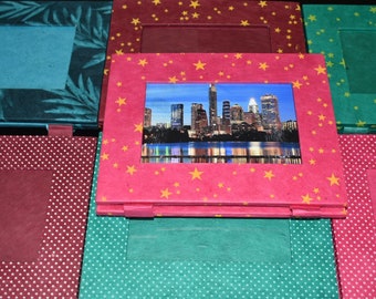 May include: A collection of handmade photo frames in various colors and patterns. One frame displays a cityscape image, set against a pink frame adorned with yellow stars. Other frames feature teal, burgundy, and polka dot designs.