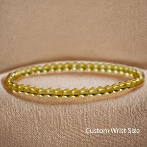 May include: A golden yellow beaded bracelet. The bracelet is made of small, round beads and is displayed on a beige fabric. The text "Custom Wrist Size" is visible in the image.