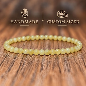 May include: A single-strand bracelet composed of small, round, pale yellow beads. Above the bracelet, the text reads HANDMADE and CUSTOM SIZED, accompanied by a hand icon with a heart and a measuring tape icon, all in a light gold color.