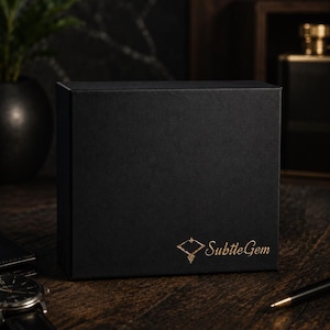 May include: A rectangular black gift box featuring the gold-colored text SubtleGem and a diamond-shaped logo on the front. The text Gift Ready Packaging is printed in gold at the bottom. The box has a smooth matte finish and a structured design.