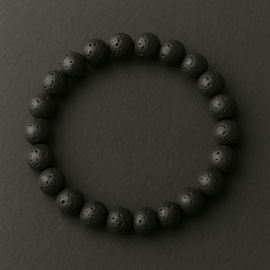 May include: A black lava stone bracelet. The bracelet is made of round, porous beads. The beads are strung together to form a circular shape. The bracelet is displayed on a dark background.