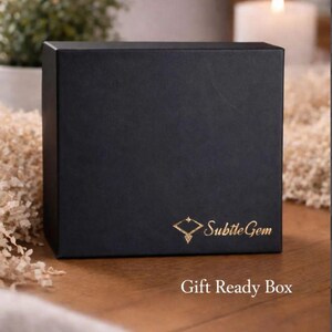 A black gift box with gold text and logo, placed on a wooden surface with a lit candle in the background.