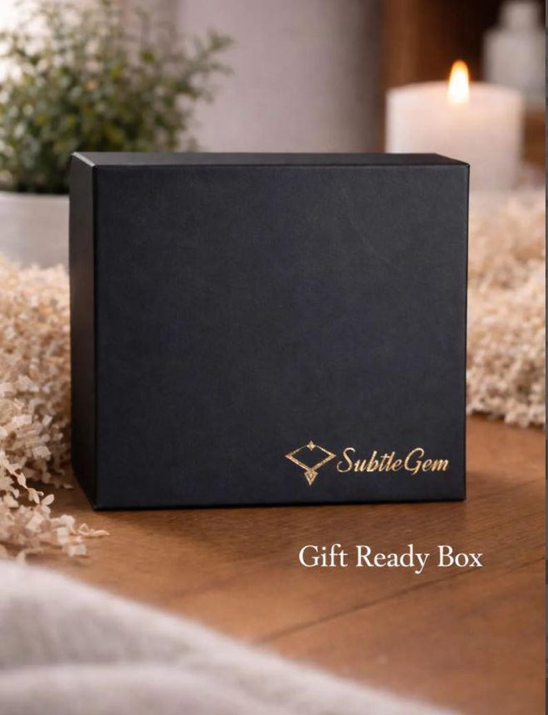 A black gift box with gold text and logo, placed on a wooden surface with a lit candle in the background.