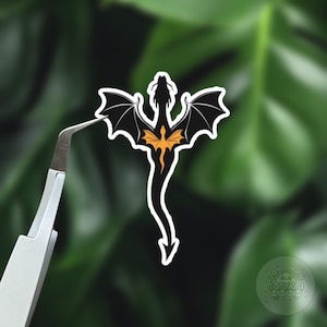 Puede incluir: Pegatina de dragón negro y naranja con las alas extendidas. El dragón está volando hacia arriba con la cola arrastrando detrás de él.