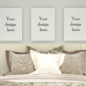 Könnte beinhalten: Drei weiße Bilderrahmen mit dem Text "Your design here" hängen an einer weißen Wand über einem Bett mit einem weißen Kopfteil und beige-braunen gemusterten Kissen.