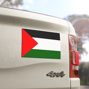 Könnte beinhalten: Ein weißer Pickup mit einem palästinensischen Flaggenmagneten auf der Ladefläche. Die Flagge ist rot, schwarz, grün und weiß.
