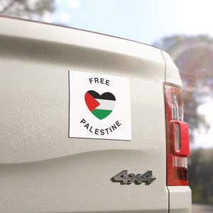 以下が含まれることがあります： 「FREE PALESTINE」と書いてある白黒のステッカーが貼られた白い車。ステッカーの中にはハート型の Palestinian フラッグが入っています。