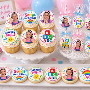 May include: A collection of cupcakes and round cookies decorated with Songs for Littles themed toppers. The designs feature a person in overalls, colorful rainbows, ABC blocks, a yellow sun, and text including Songs for Littles and Can you say.