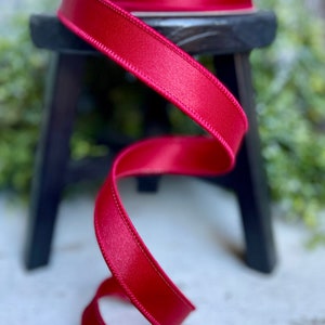 May include: A spool of red satin ribbon with a wired edge. The ribbon is coiled on a wooden stool.