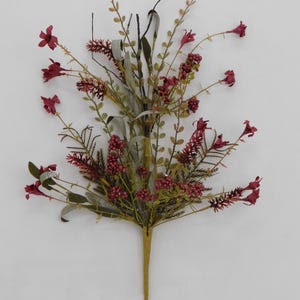 May include: A decorative floral spray featuring deep burgundy trumpet-shaped flowers, clusters of small red berries, and various green foliage stems. The arrangement is gathered onto a single, light-colored central stem at the base.
