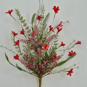 May include: A vibrant artificial floral arrangement featuring bright red flowers, green leaves, and delicate pink accents. The bouquet has a brown stem and is set against a plain white background. Ideal for home decor or crafting.