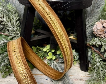 May include: A spool of brown velvet ribbon featuring a central metallic gold woven trim. The ribbon has a soft, textured surface and a shimmering gold stripe running down the middle, providing a decorative edge and a consistent, elegant appearance.