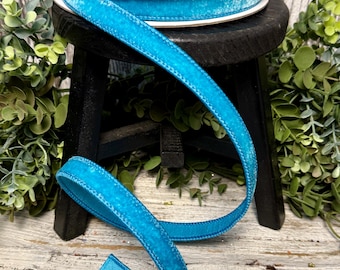May include: A spool of turquoise blue velvet ribbon with a white stitching detail. The ribbon is on a black spool with the word "Farrisilk" printed on it.