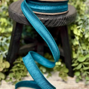Peut inclure: Ruban de satin turquoise avec un bord cousu. Le ruban est enroul&eacute; sur une bobine et est pos&eacute; sur un tabouret en bois.