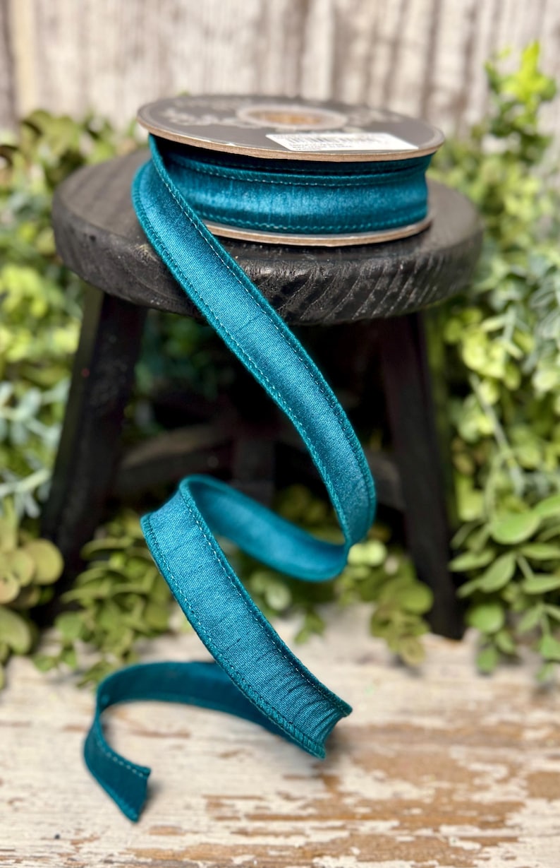 Peut inclure: Ruban de satin turquoise avec un bord cousu. Le ruban est enroul&eacute; sur une bobine et est pos&eacute; sur un tabouret en bois.