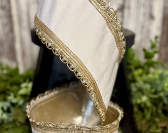 May include: Two off-white fabric lamp shades with gold trim and pearl accents. The shades are stacked, with the top one angled. The top of the shade is dark brown.