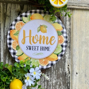 Może przedstawiać: Wieniec w czarno-białe kratę z okrągłym znakiem, na kt&oacute;rym napisano "Home Sweet Home", otoczony cytrynami i limonkami. Wieniec jest ozdobiony białymi kwiatami i zielonymi liśćmi.