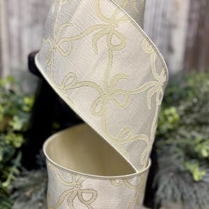 May include: A roll of decorative ribbon with a cream-colored background and a repeating pattern of light gold bows. The ribbon is made of a textured fabric and is ideal for crafts, gift wrapping, or holiday decorations.
