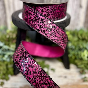 May include: A roll of decorative ribbon with a vibrant pink and black glitter design. The ribbon is displayed in a flowing, curled arrangement, showcasing its texture and color. The ribbon is likely used for crafts, gift wrapping, or event decorations.