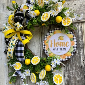 Może przedstawiać: Wianek w kształcie cytryny z czarno-białą wstążką w kratkę, białymi stokrotkami i tabliczką z napisem "Home Sweet Home".