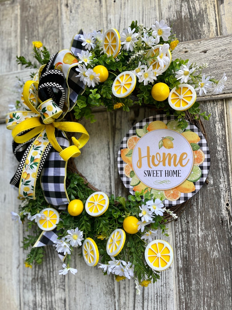 Może przedstawiać: Wianek w kształcie cytryny z czarno-białą wstążką w kratkę, białymi stokrotkami i tabliczką z napisem "Home Sweet Home".