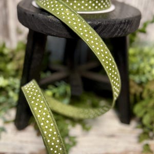 May include: Green ribbon with white polka dots, unspooled and resting on a small black stool. A roll of the same ribbon sits on top of the stool. The ribbon is a decorative element, suitable for crafts and gift wrapping.