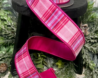 Pode incluir: Um carretel de fita aramada com um padrão xadrez em rosa, roxo e branco. A fita tem um verso acetinado em rosa fúcsia vibrante e bordas costuradas a condizer, criando um contraste distinto com o design xadrez mais claro da fita.