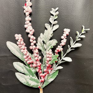 May include: Artificial floral stem featuring red berries and green leaves dusted with white. The stem has a brown base and is designed for decorative purposes. The berries are clustered along the stem, and the leaves have a realistic texture.