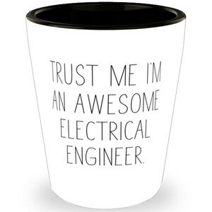 May include: White shot glass with a black rim. The text "TRUST ME I'M AN AWESOME ELECTRICAL ENGINEER" is printed in black. The glass has a tapered design.