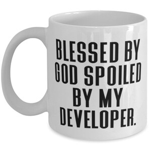 Puede incluir: Taza de café de cerámica blanca con texto negro que dice "Blessed by God Spoiled by My Developer."
