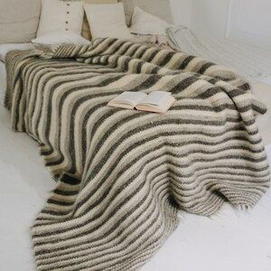 May include: A white bed with a striped gray and white blanket and a book on top. The bed has several pillows in various shades of beige and white.